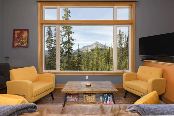 Living room with yellow armchairs, wood coffee table, and large windows framing mountain and forest views